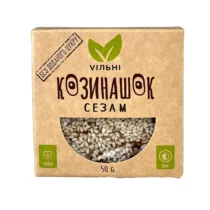 Brown cardboard sesame seeds package with a clear window showing white sesame seeds and green vegan/raw icons; 50 g label visible.