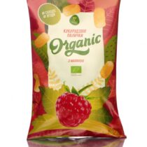 Front of pink and green bag of Organic corn sticks with raspberry flavor, featuring a raspberry image and leaves, standing upright with reflection.